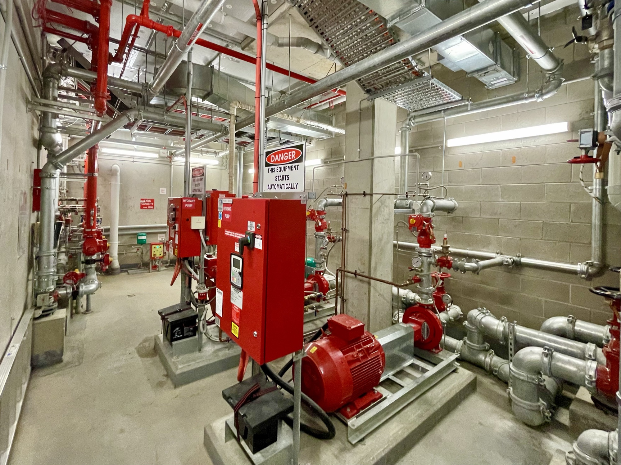 A fire pump room: red hydrant pump and jockey pump, control panels and painted steel pipework running to the ceiling.